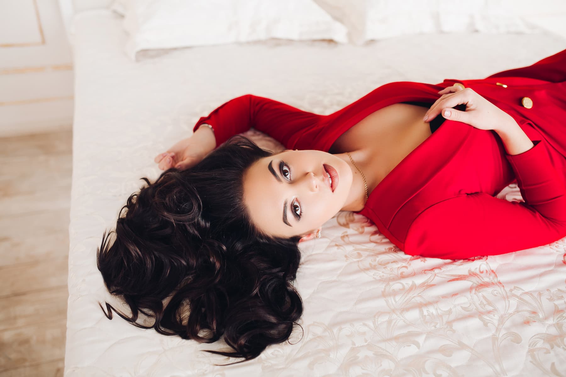 Ragazza sexy in abito rosso sdraiata sul letto con gli occhi marroni.